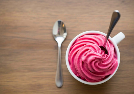 A pink dessert in a white mug with a spoon on a wooden tableの写真素材