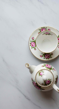 A delicate floral teapot and cup on a marble surface