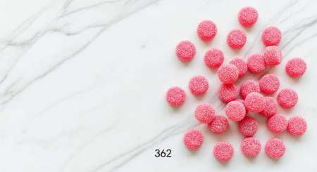 Pile of pink candies with sparkling sugar coating on white marble background
