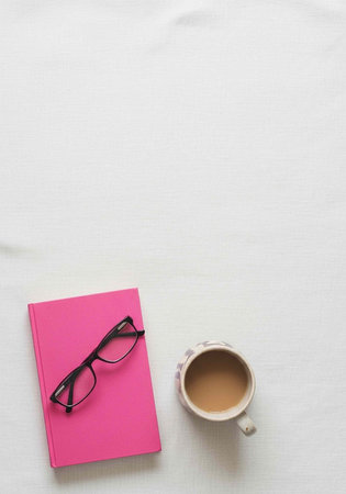 A pink notebook with black glasses and a coffee cup on a white surface