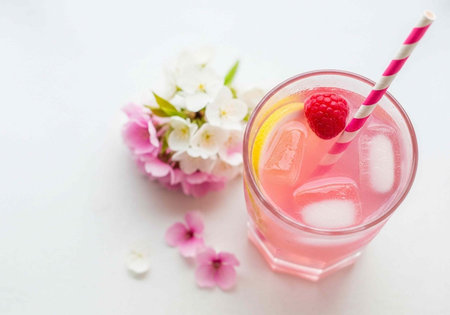 Pink beverage in a glass with ice, raspberry, and straw, surrounded by flowers