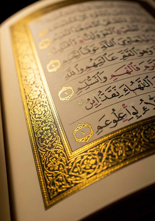 A close-up view of an open book with Arabic calligraphy and gold ornate designs on a dark background