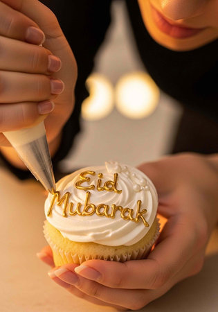 A person decorating a cupcake with Eid Mubarak message in golden icing for a festive celebration