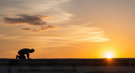A person in silhouette kneels on a rooftop against a bright orange sunset with scattered clouds