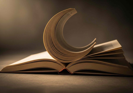 Book lying open with curved pages, illuminated by warm light on a dark surfaceの写真素材