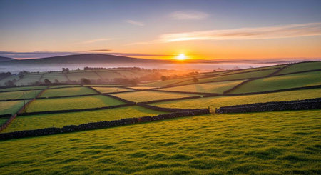 A serene landscape of green fields and rolling hills at sunrise or sunset with a clear blue skyの写真素材