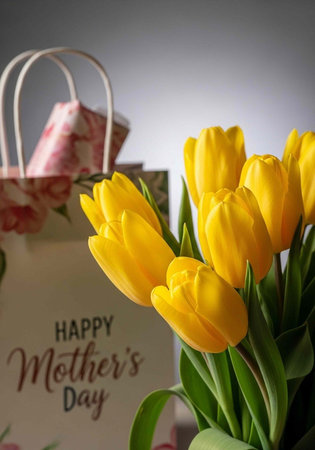 A bouquet of bright yellow tulips with a Happy Mother's Day card and gift bag in the background