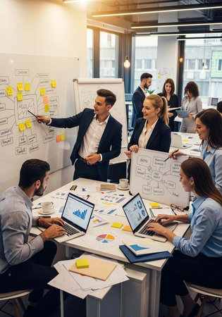 A group of business professionals engaged in a meeting with laptops and whiteboards in a modern...