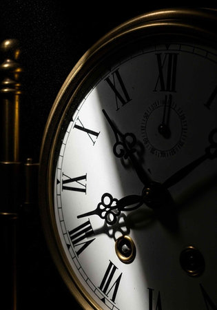 A close-up of an antique clock with Roman numerals and a golden frame in a dark setting