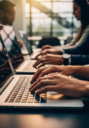 Hands of multiple individuals typing on laptops in a row, with a blurred background of an office...