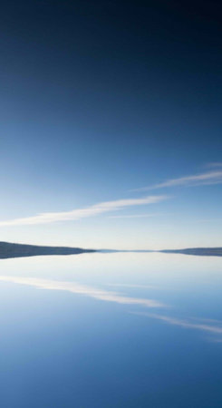 A serene landscape of a calm body of water under a clear blue sky with wispy cloudsの写真素材