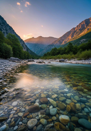 A serene mountain river flows gently through a rocky landscape at sunset