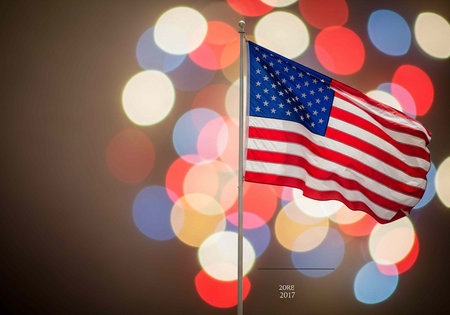 The American flag waving proudly in front of a vibrant colorful bokeh light background at night