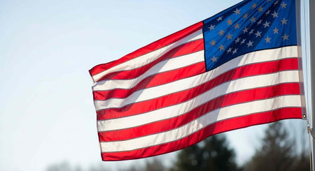 The American flag waving in the wind on a clear day with trees in the background.