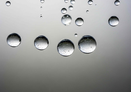 Clear water droplets of different sizes on a gray background, reflecting light and showcasing...