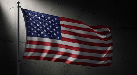 A US flag flies on a pole against a cracked concrete wall with spotlight illumination