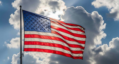 The United States flag flies high with red, white, and blue colors against a cloudy sky