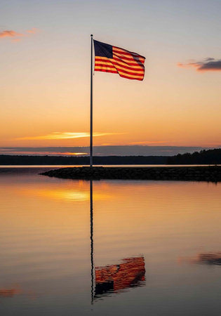 A serene American flag scene at sunset with a flagpole and reflection in calm waterの写真素材