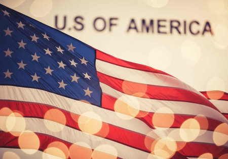 Close-up of waving American flag with stars and stripes, U.S. of America text, and bokeh lights