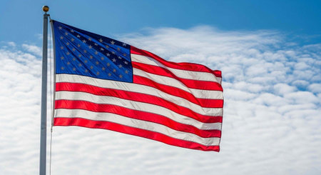 The United States flag flies on a pole against a partly cloudy sky.