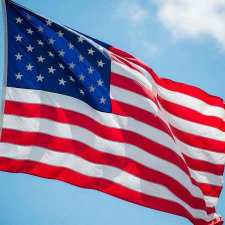 A large American flag flying with red and white stripes and white stars on blue sky