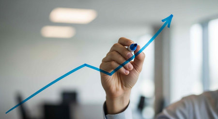 A hand drawing a blue upward trend line with a marker in a modern office setting.