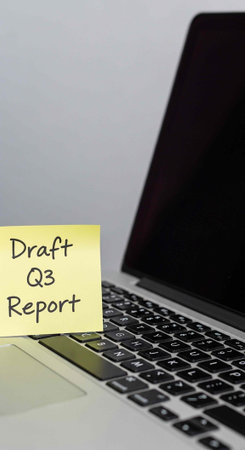 A laptop with a yellow sticky note that reads Draft Q3 Report on a plain background
