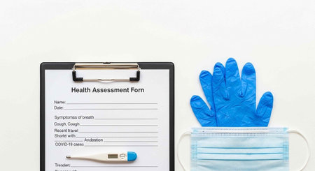 A health assessment form on a clipboard with a thermometer, blue gloves, and a face mask on a white...