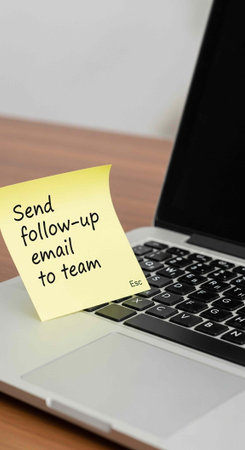 Laptop with black keyboard and yellow sticky note reminder on wooden desk
