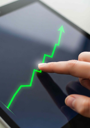 Close-up of hand touching tablet with green graph line trending upward on screen