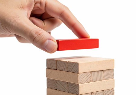 A hand carefully placing a red block on top of a stack of wooden blocksの写真素材