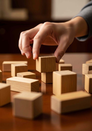 A person's hand building a structure with wooden blocks on a table
