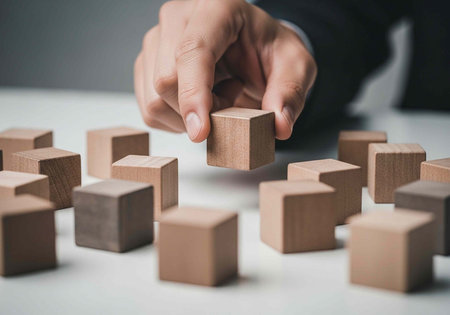A person's hand placing a wooden block among many others on a table