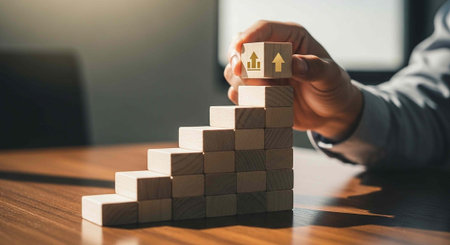 A person building a staircase of wooden blocks with an upward arrow on top in a modern office...