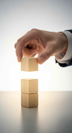 A hand in a business suit placing a wooden block on top of two stacked blocks