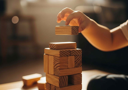 A person's hand carefully placing a wooden block on top of a tower of blocks