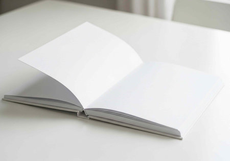 An open blank book lying on a white table with natural light shining in from the side