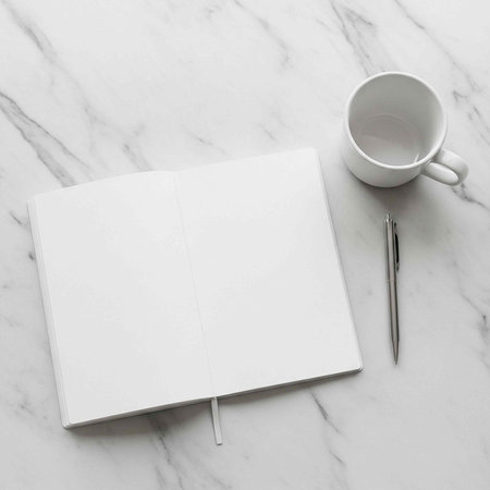 A white notebook, pen, and coffee cup on a marble surface for writing and creativity