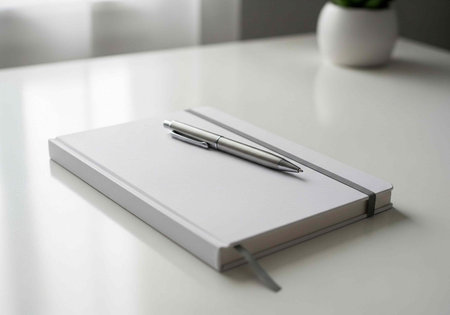 A silver pen rests on a closed white notebook with a elastic band on a clean desk surface