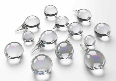 Collection of transparent glass objects in spherical and teardrop forms, scattered on a plain white...
