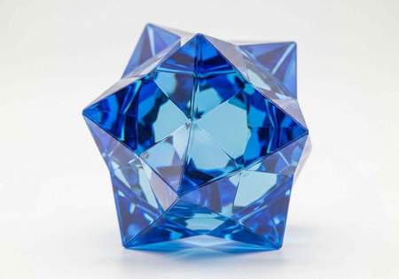 A blue crystal object with many geometric facets and reflections sits on a plain white surface and backgroundの写真素材