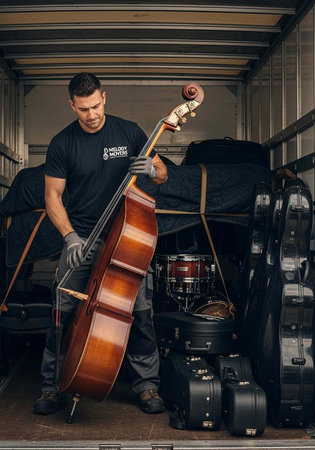 Man in black shirt holding double bass in moving truck with musical gear