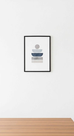 A minimalist framed abstract art piece hangs on a white wall above a wooden table