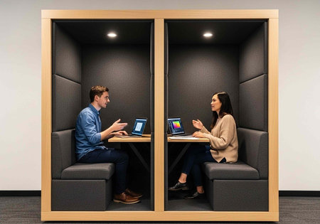 A man and woman working on laptops in a modern office with soundproof booths for privacy and focus