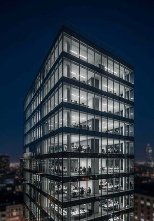 A modern office building with glass windows lit up at night in a bustling cityscape