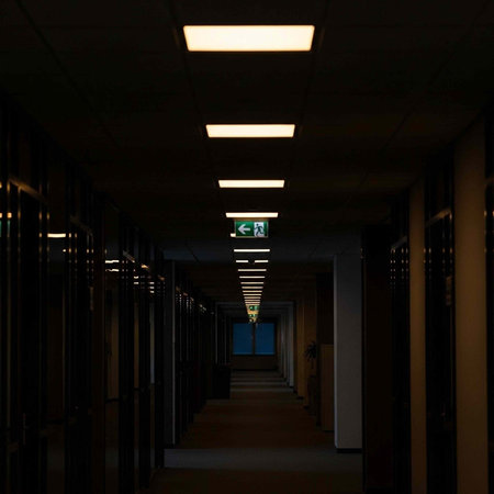 A dimly lit hospital corridor with fluorescent lights and a green exit sign leading to a blue door