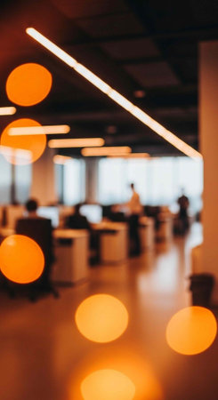A modern office space with sleek lighting and a blurred background of employees at workstations
