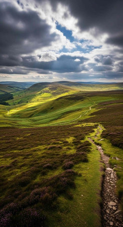 A serene landscape of rolling hills and green fields under a cloudy sky with a winding stone pathの写真素材