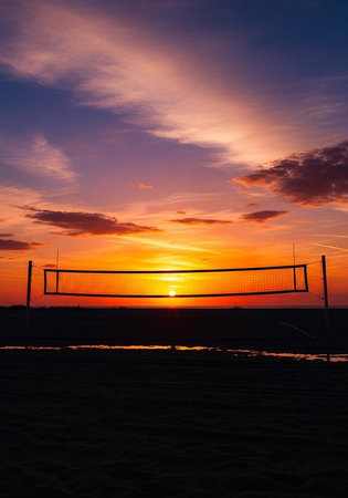 A serene beach volleyball net at sunset with a vibrant sky and peaceful atmosphereの写真素材