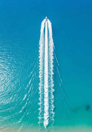 Aerial view of a boat speeding across the ocean leaving a trail of white water in its wake